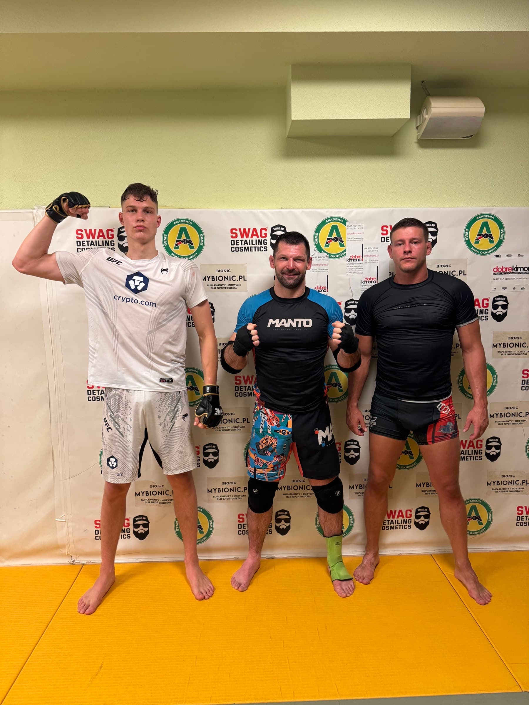 Trzej zawodnicy po treningu MMA przed banerem Akademii