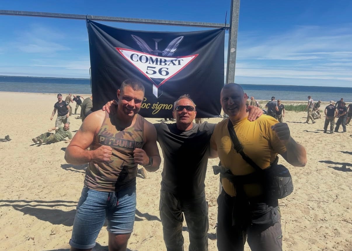 Od lewej Adam Okniński, mjr Arkadiusz Kups i Mirosław Okniński na plaży pod banerem Combat 56, w tle uczestnicy szkolenia ćwiczący na piasku