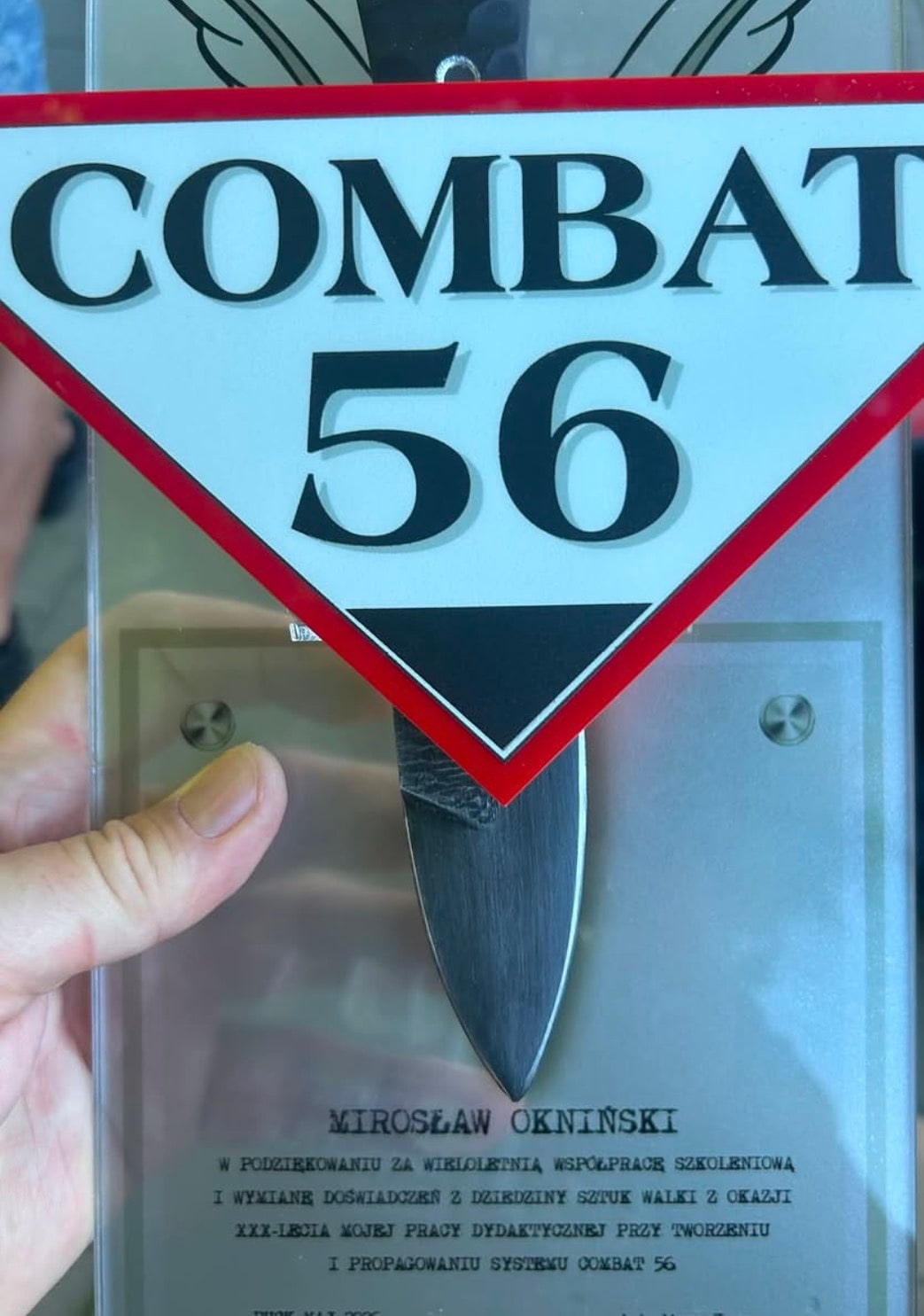 Pamiątkowa tablica Combat 56 z nożem i napisem: Mirosław Okniński, w podziękowaniu za wieloletnią współpracę szkoleniową i wymianę doświadczeń z dziedziny sztuk walki z okazji XXX-lecia mojej pracy dydaktycznej przy tworzeniu i propagowaniu systemu Combat 56.