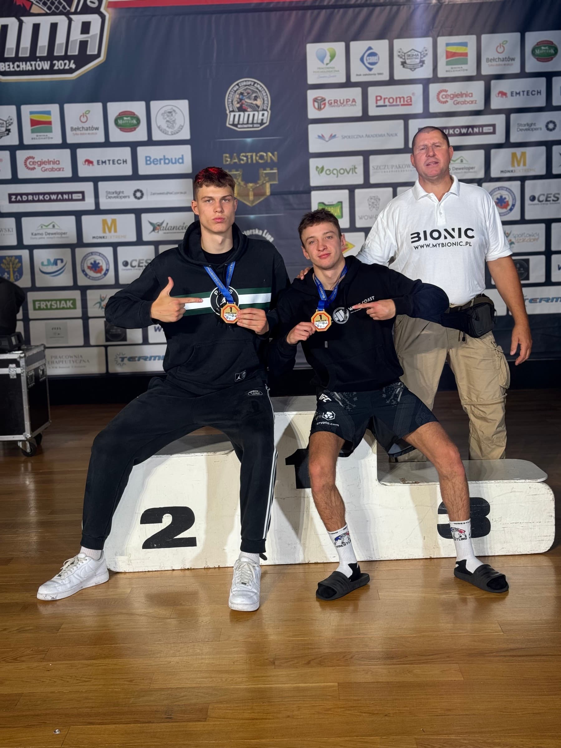 Krystian Jakowicz i Aleksander Okniński ze złotymi medalami przy podium, obok Mirosław Okniński
